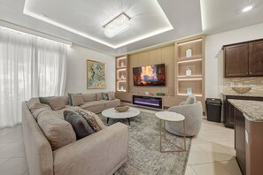 Ein modernes Wohnzimmer mit einer großen Couch, einem Flachbildfernseher, einem Kamin und einer Küchenzeile.