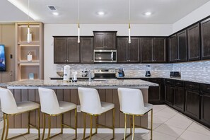 A modern kitchen with dark wood cabinets, a large island with bar stools, stainless steel appliances, and a tiled backsplash. - 10BR house at Windsor Cay Resort (Clermont)
