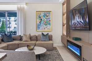 Una sala de estar moderna con un sofá seccional, un televisor de pantalla plana, una chimenea y un cuadro abstracto grande.