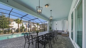 A covered patio with a pool, outdoor seating, and a view of neighboring houses. - 10BR house at Windsor Cay Resort (Clermont)