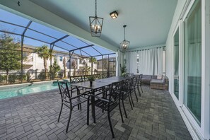 Eine überdachte Terrasse mit Pool, Sitzgelegenheiten im Freien und Blick auf umliegende Häuser.