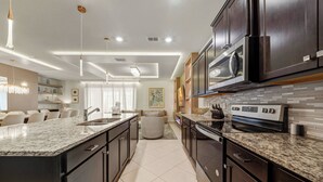 A modern kitchen with dark cabinetry, granite countertops, stainless steel appliances, and pendant lighting. - 10BR house at Windsor Cay Resort (Clermont)