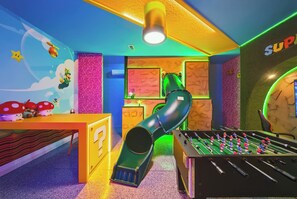 A room with a foosball table, a slide, and a wall with a Mario character. - 10BR house with private pool and game room (Clermont)