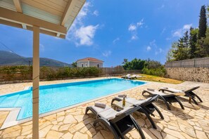 Una piscina con lettini, una pergola e un muro in pietra.