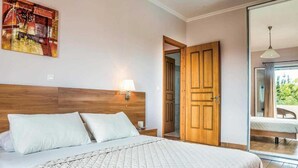 Un dormitorio con una cama grande, un cabecero de madera, una lámpara de pared, una puerta que da a un balcón y un cuadro en la pared.