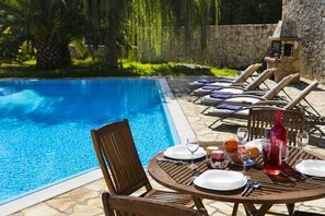 Area ristoro a bordo piscina con tavolo apparecchiato per due, circondata da poltrone relax.