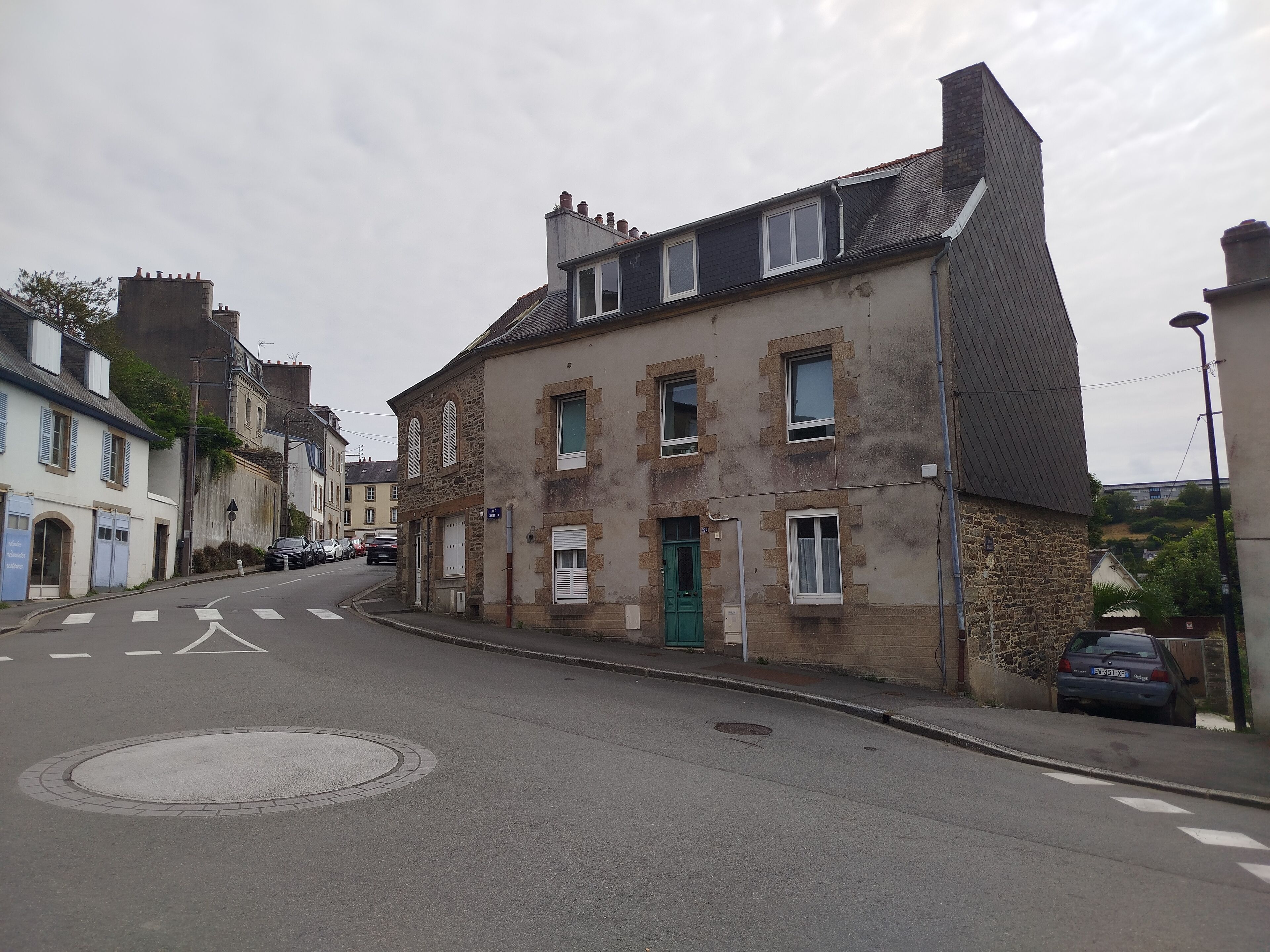 A street with buildings, a roundabout, and parked cars.
