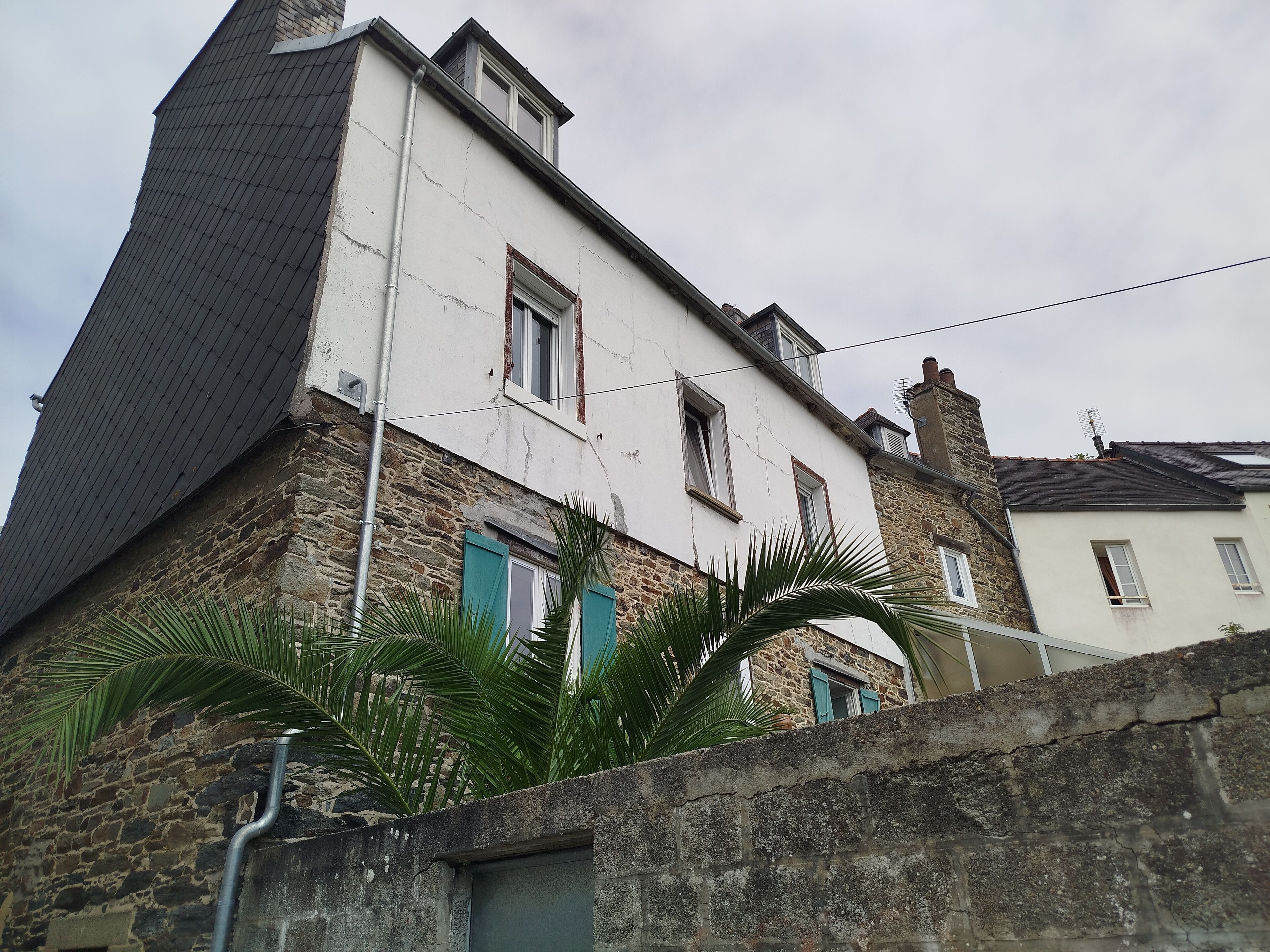 A two-story building with stone walls and a white facade, featuring multiple windows with shutters.