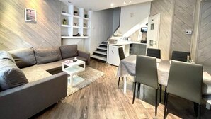 Een moderne leefruimte met een bank, eettafel en trap naar een keuken.