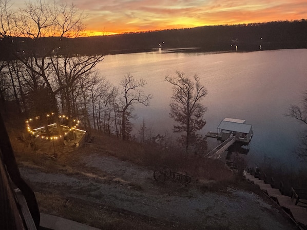 Vista al lago al atardecer con un muelle y un árbol decorado con luces.