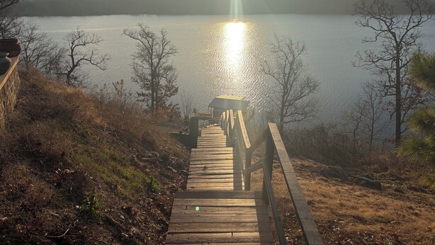 A wooden boardwalk leading to a dock over a calm lake, surrounded by trees and a forested hill.