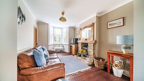A cozy living room with a leather sofa, a fireplace, and a wooden table. - Sunnydene - sleeps 6 guests  in 3 bedrooms (Brancaster Staithe)