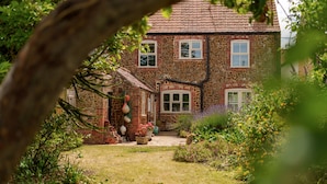A stone house with a tiled roof, a brick pathway leading to the entrance, and a garden with various plants and flowers. - Sunnydene - sleeps 6 guests  in 3 bedrooms (Brancaster Staithe)