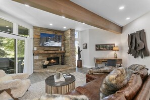A modern living room with a stone fireplace, leather furniture, and a large TV. - Elegant Deer Valley 2BR-Private Hot Tub-Walk to Deer Valley Resort (Park City)
