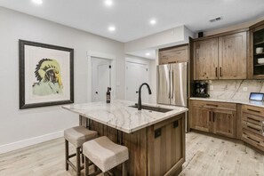A kitchen with a marble island, wooden cabinets, and a framed artwork on the wall. - Elegant Deer Valley 2BR-Private Hot Tub-Walk to Deer Valley Resort (Park City)