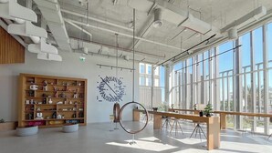 Een ruim, modern interieur met een grote houten boekenkast, een rondhangende sculptuur en een lange houten tafel.