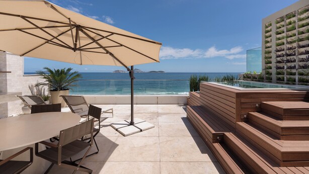 Una terrazza con tavolo, sedie e ombrellone che si affaccia su una piscina e l'oceano.