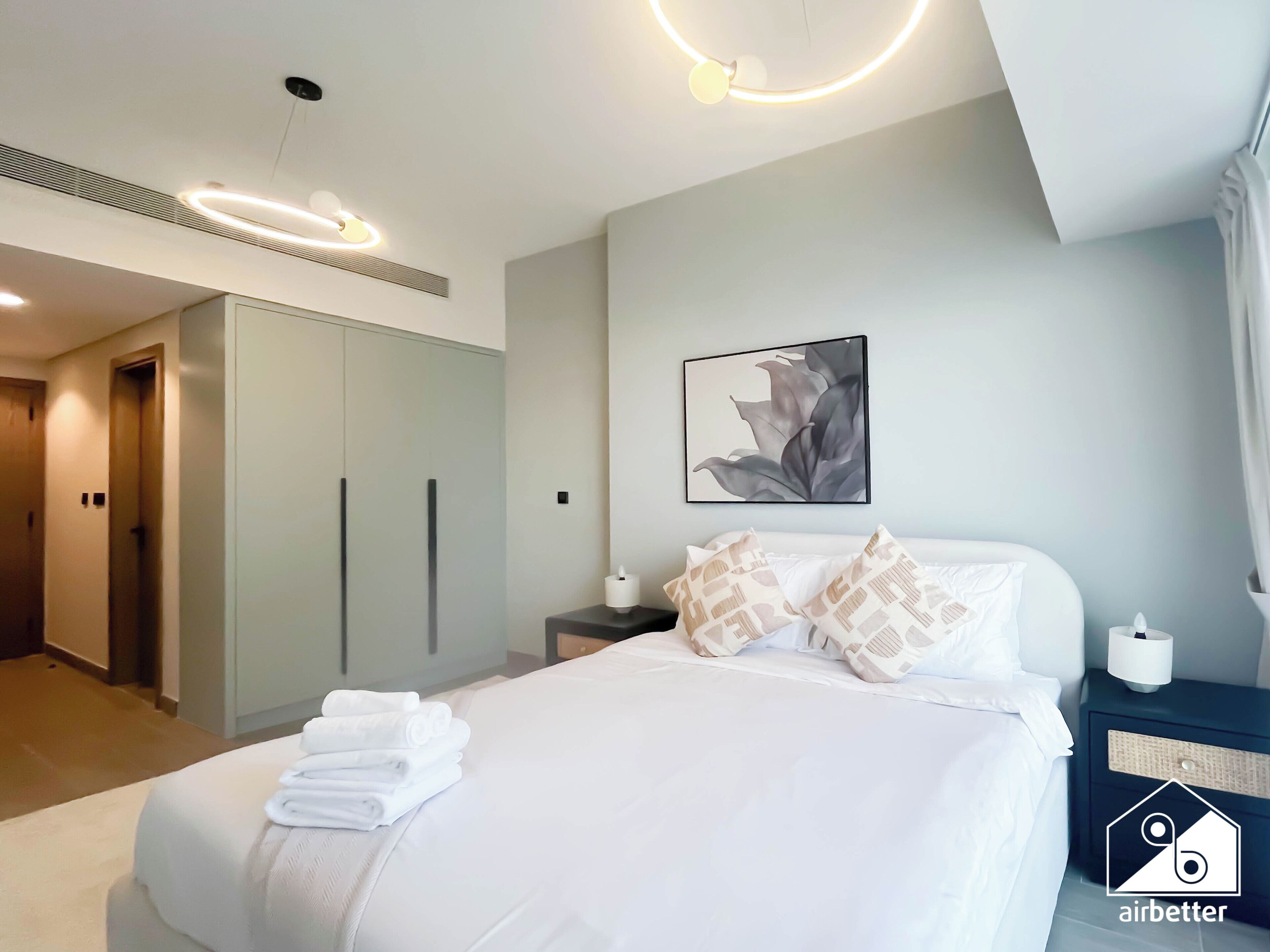 A modern hotel room with a neatly made bed, a large wardrobe, a bedside table with a lamp, and a wall-mounted artwork.