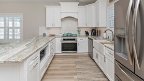 A modern kitchen with white cabinetry, a marble countertop, stainless steel appliances, and a wooden floor. - Coastal Comfort ~ your own Heated Pool ~ Golf Cart (North Myrtle Beach)