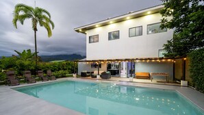 Ett modernt hus i två våningar med en swimmingpool, en uteplats och utsikt över bergen.