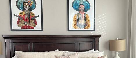 A neatly made bed with patterned pillows, a wooden bench, and two framed artworks on the wall.