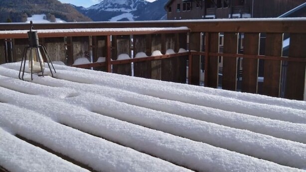 Un ponte innevato con ringhiera in legno, un treppiede e una vista sulle montagne sullo sfondo.