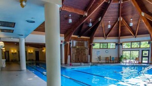 Ein Hallenbad mit Holzbalken, deutlich abgetrennten Bahnen und einem Sitzbereich mit Stühlen.