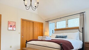 Ein Schlafzimmer mit Bett, Nachttisch, Bank und einem Fenster mit Vorhängen.