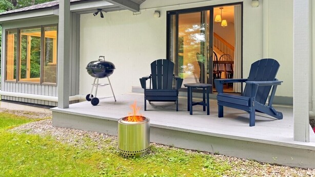 Eine überdachte Veranda mit Grill, zwei Adirondack-Stühlen und einer Feuerstelle.