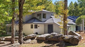 Ein modernes, zweistöckiges Haus mit einer Veranda, umgeben von großen Steinen und Bäumen.