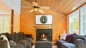 A cozy living room with a fireplace, wooden walls, and a ceiling fan. - Mountain Moose Chalet- indoor hot tub, FirePit (Killington)