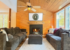 A cozy living room with a fireplace, wooden walls, and a ceiling fan. - Mountain Moose Chalet- indoor hot tub, FirePit (Killington)