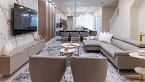 Ein modernes Wohnzimmer mit einem Ecksofa, einem an der Wand montierten Fernseher und einem Essbereich mit rundem Tisch und Stühlen.