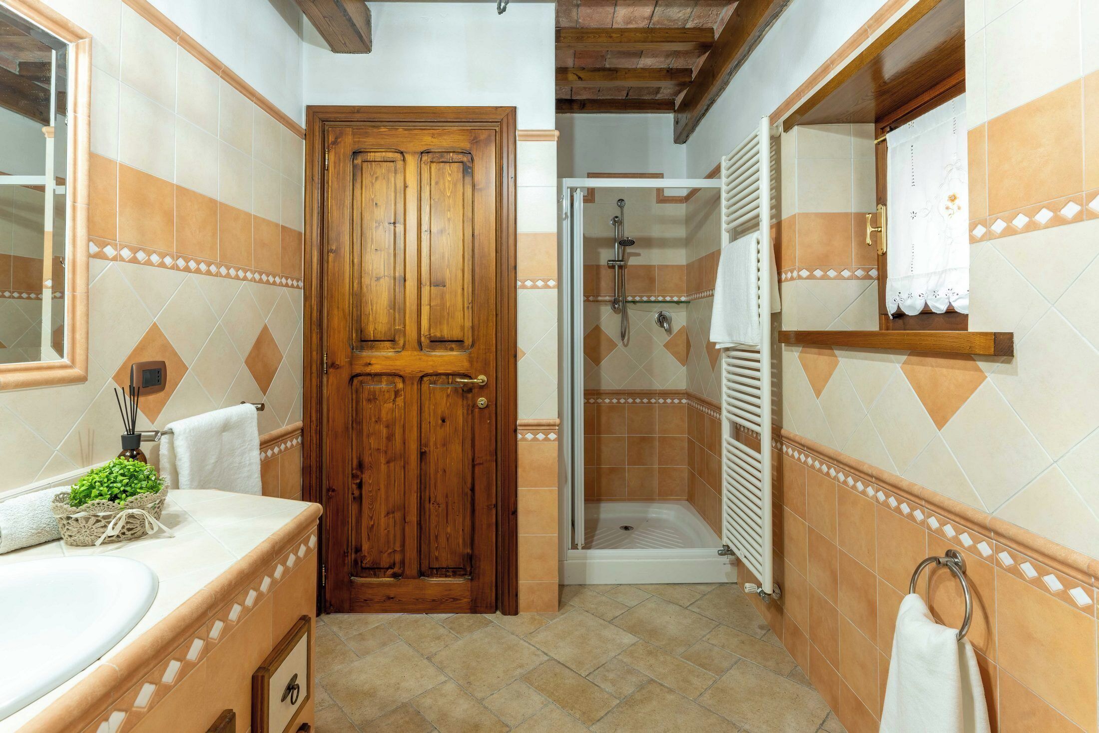 A bathroom with a wooden door, a shower, and a sink with a towel rack.