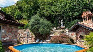 Un edificio de piedra con piscina, mobiliario exterior y una estatua.