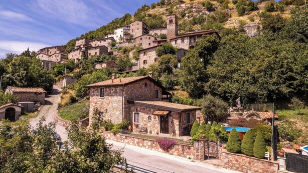 Un pueblo en la ladera con edificios de piedra, un camino serpenteante y una estatua en primer plano.