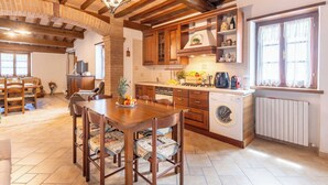 Una cocina rústica con armarios de madera, una mesa de comedor con sillas, una lavadora y una ventana con cortinas de encaje.