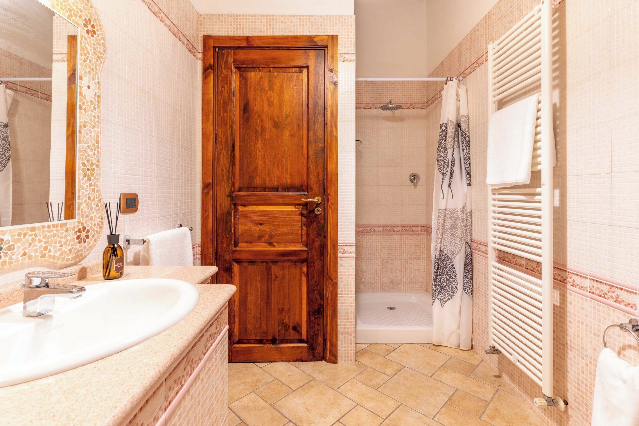 Un baño con puerta de madera, lavamanos, ducha y un perchero para toallas.