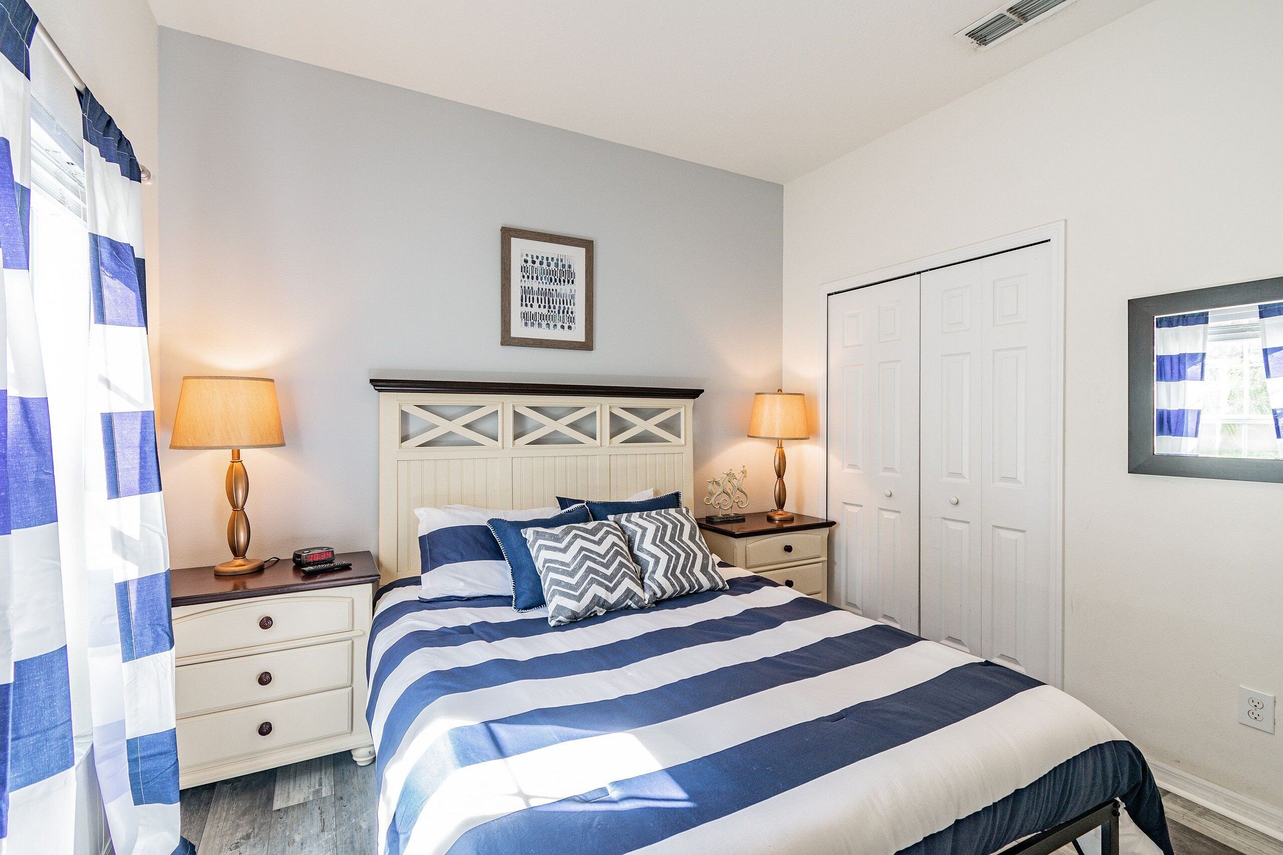 A bedroom with a bed, two bedside tables with lamps, a white door, and a framed picture on the wall.