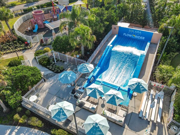 Ein Swimmingpool mit Wasserrutsche, umgeben von Liegestühlen und Sonnenschirmen, sowie ein Spielbereich.