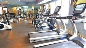Ein Fitnessstudio mit mehreren Laufbändern, Kraftgeräten und einem digitalen Bildschirm.