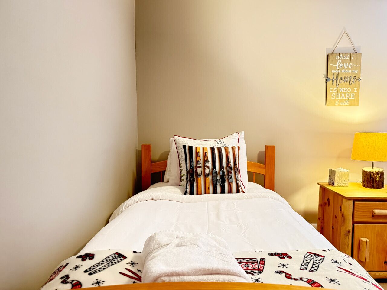 A neatly made bed with a white duvet and patterned bedding, a wooden headboard, and a bedside table with a lamp and a small decorative item.