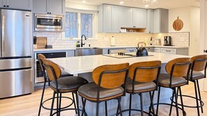 A modern kitchen with a central island, stainless steel appliances, and bar stools. - Sunset Notch- Hot tub, Cold Plunge, Hiking, Views! (Mendon)