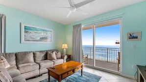 A living room with a sofa, coffee table, and a view of the ocean through a sliding glass door. - 🏖️Beachfront | Gulf Views | Incredible Interior | 3BR Sterling Reef 301🏖️ (Panama City Beach)
