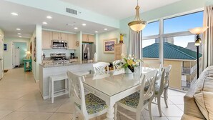 A spacious kitchen with modern appliances, a dining area with a glass table, and large windows offering a view of the city. - 🏖️Beachfront | Gulf Views | Incredible Interior | 3BR Sterling Reef 301🏖️ (Panama City Beach)