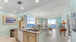 A spacious kitchen with a large island, a dining area with a view, and a living room with a balcony. - 🏖️Beachfront | Gulf Views | Incredible Interior | 3BR Sterling Reef 301🏖️ (Panama City Beach)