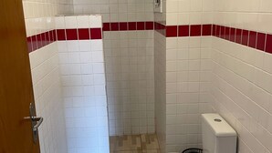 A bathroom with white tiled walls, a shower, a toilet, and a bidet. - Beachfront apartment (Ubatuba)