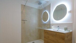 Ein modernes Badezimmer mit einer gläsernen Duschkabine, einem Holzwaschtisch mit Spiegel und einem weißen Waschbecken.