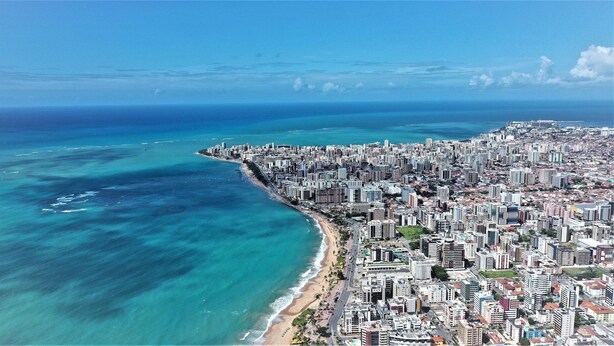 Un paisaje urbano costero con una playa, edificios densos y un cielo azul despejado.