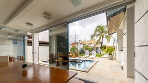 Un interior moderno con una mesa de comedor de madera, un ventanal de vidrio que da a una zona de piscina y vistas al exterior.